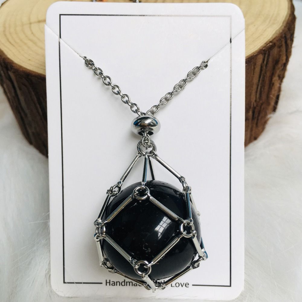 Collier argenté avec filet de maillons autour d'une pierre noire ronde et brillante, présenté sur une carte blanche et du bois. 8