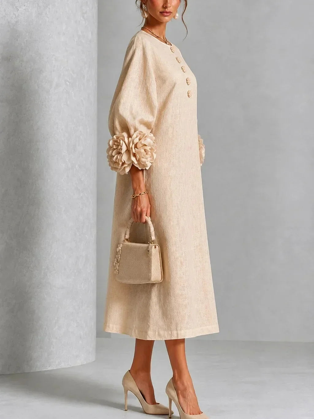 Robe beige portée de profil, montrant la coupe droite, la manche bouffante à grosse fleur au poignet et les boutons fleuris du devant. 8