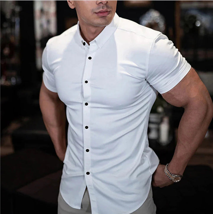 Chemise blanche à boutons noirs portée par un homme musclé, une main à la hanche, montre au poignet. 2