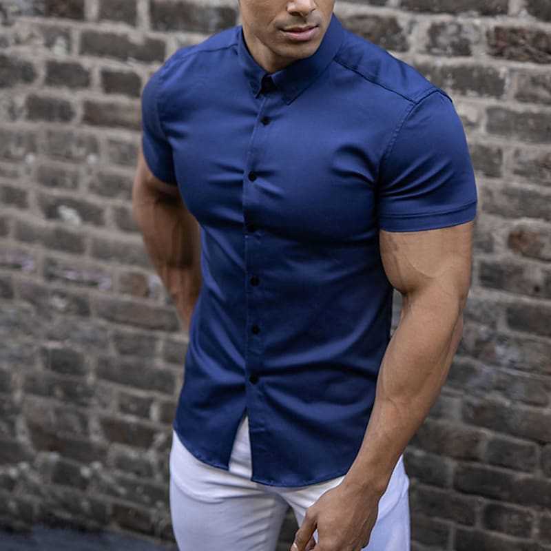 Chemise bleu marine portée avec un pantalon blanc par un homme musclé devant un mur de briques. 3