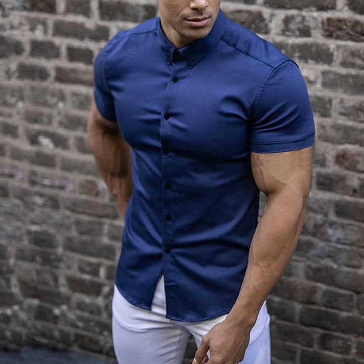 Chemise bleu marine portée avec un pantalon blanc par un homme musclé devant un mur de briques. 3