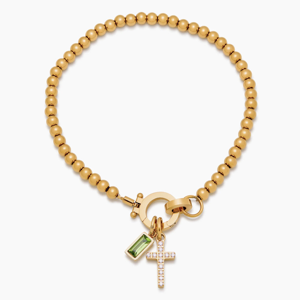 Bracelet de perles dorées posé à plat, vue de dessus, avec croix sertie de strass et pierre verte rectangulaire. 2