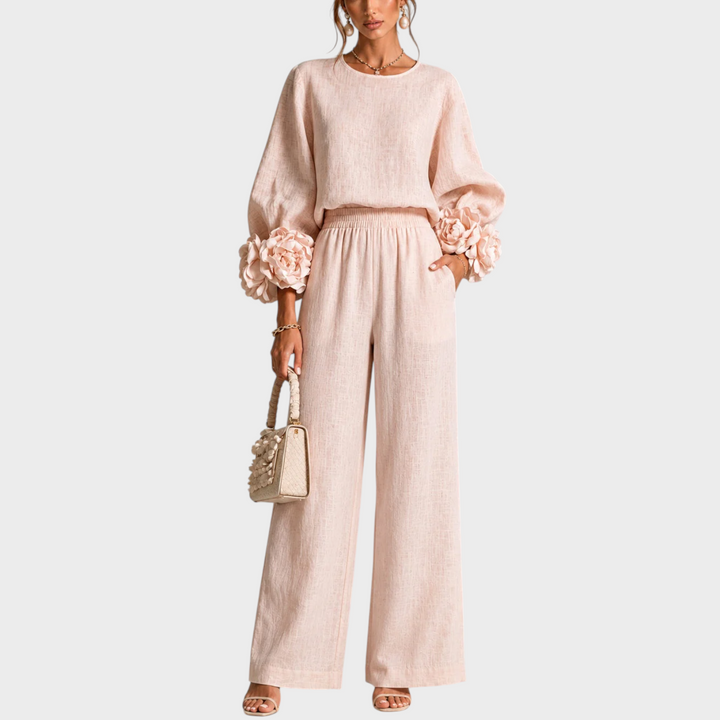 Femme de face portant l'ensemble rose pâle, manches ornées de grandes fleurs, sac beige à la main 1