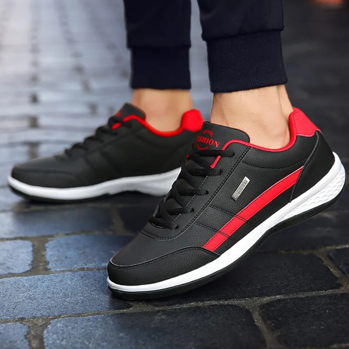 Baskets noires à bande rouge portées par un homme en pantalon sombre, marchant sur un pavage de rue. 2