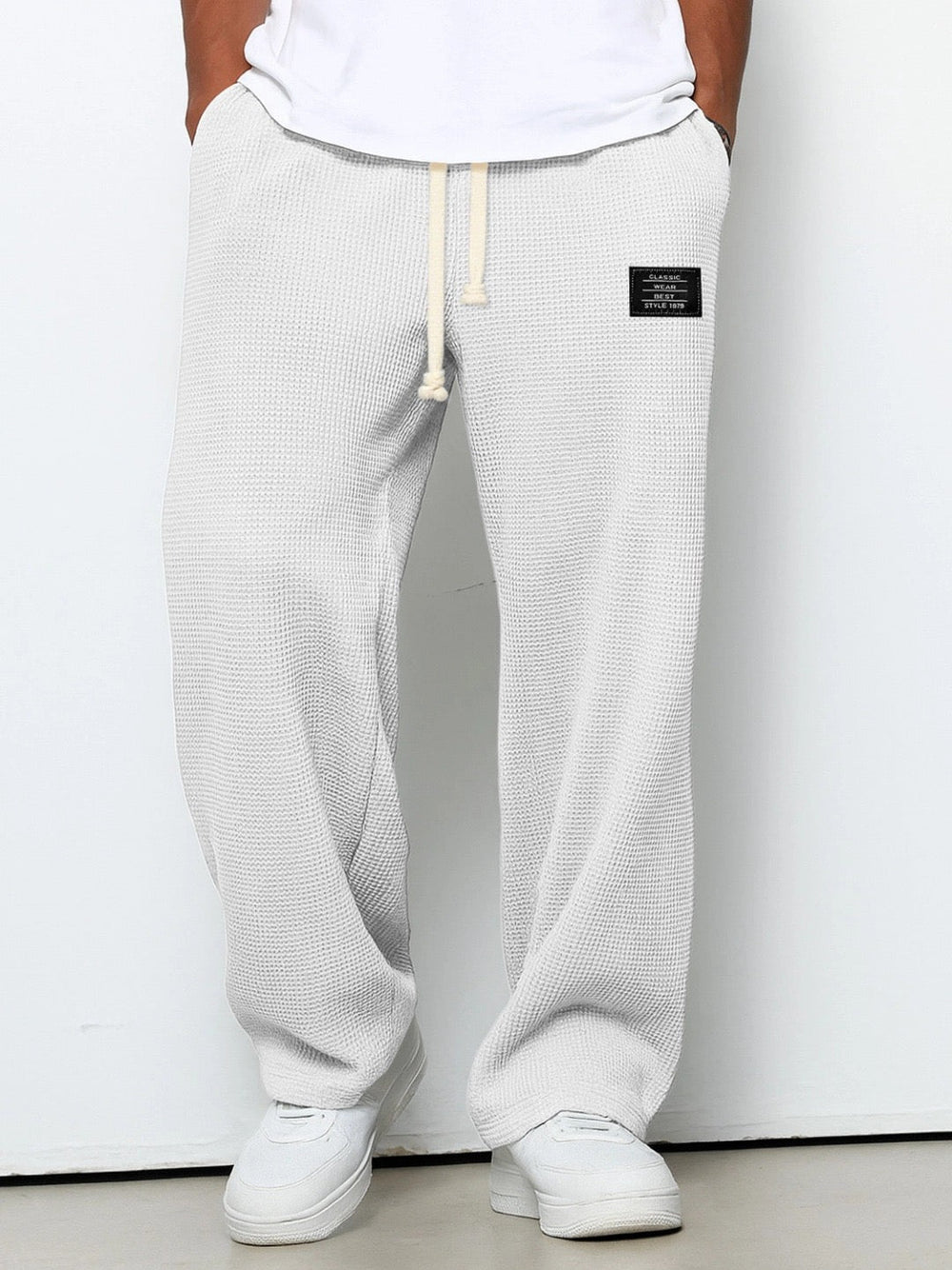Version gris très clair, presque blanche, du pantalon large en maille gaufrée, vue de face sur un modèle en baskets blanches. 2