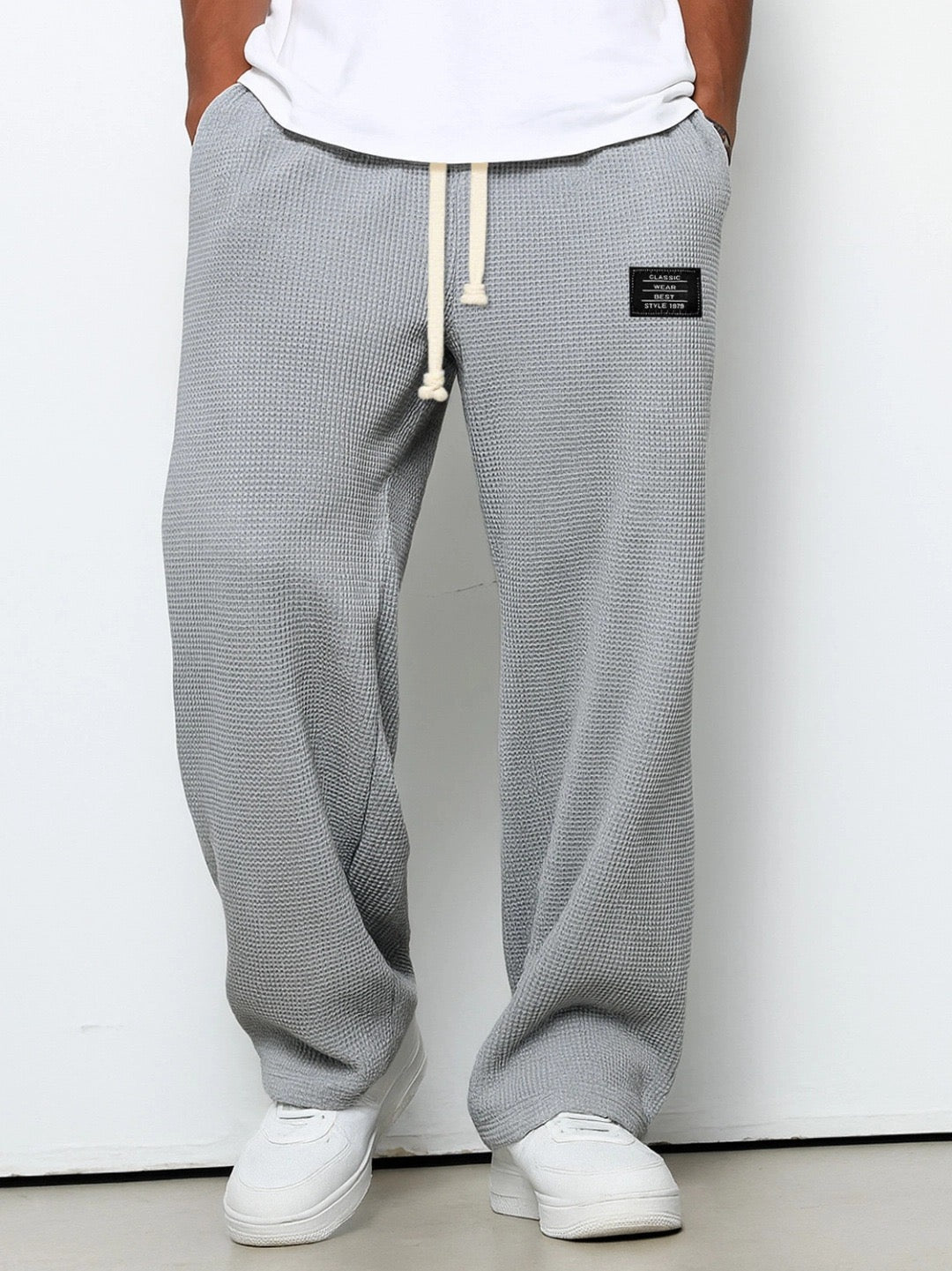 Version gris moyen du pantalon large en maille gaufrée, cordon de serrage beige, portée par un modèle devant un mur clair. 3