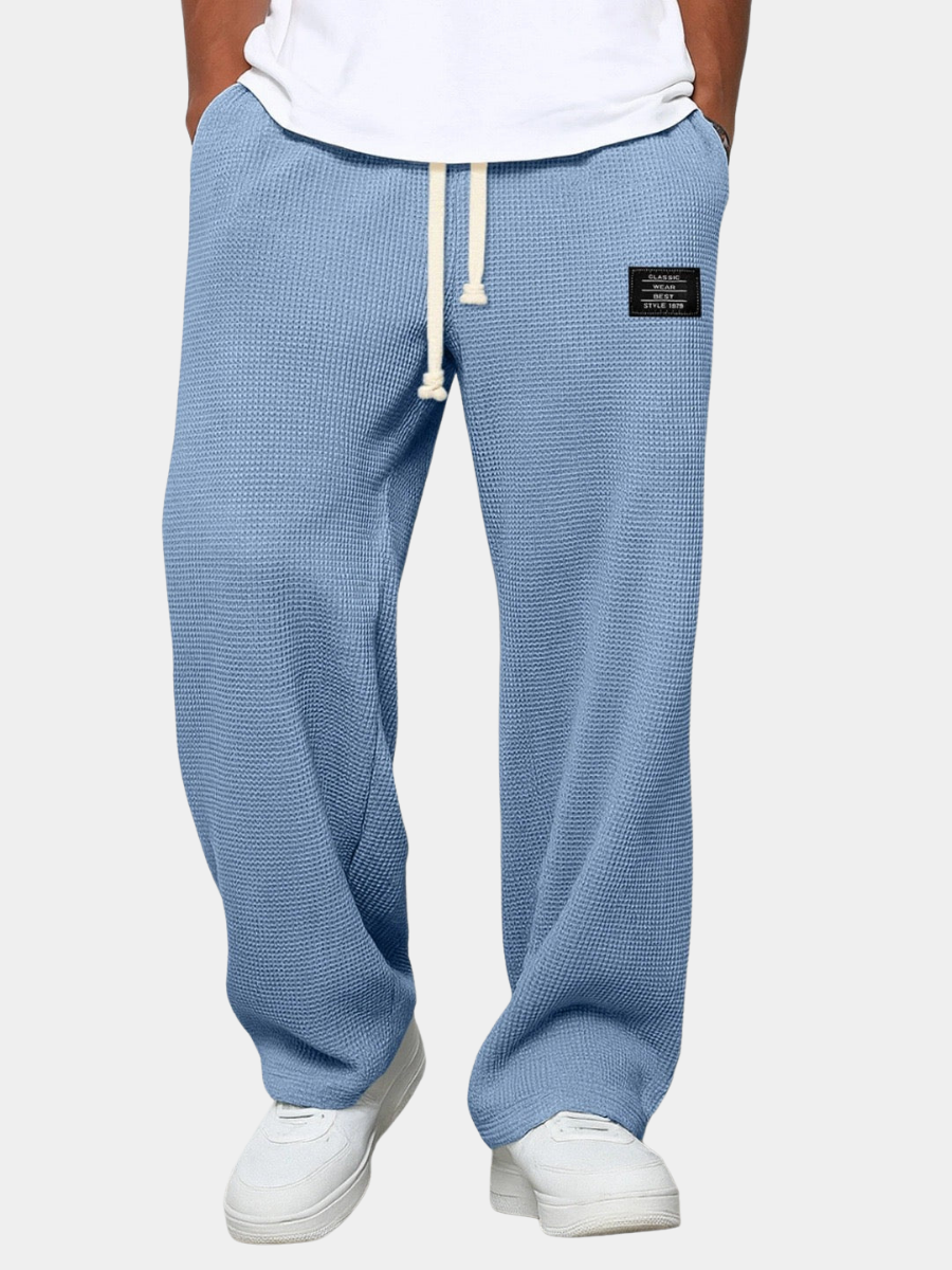 Version bleu clair du pantalon large en maille gaufrée, vue de face sur fond uni, avec cordon beige et t-shirt blanc. 4