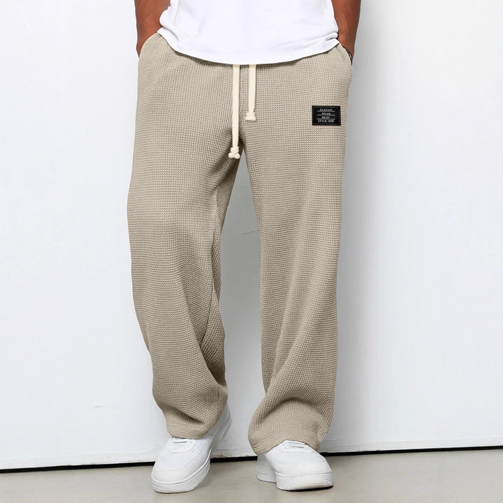 Version beige sable du pantalon large en maille gaufrée, vue de face légèrement plus rapprochée, mains dans les poches, baskets blanches. 6