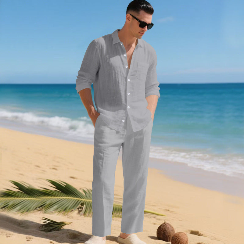 Homme sur une plage portant l'ensemble chemise à manches longues et pantalon droit en gris clair, lunettes de soleil. 2