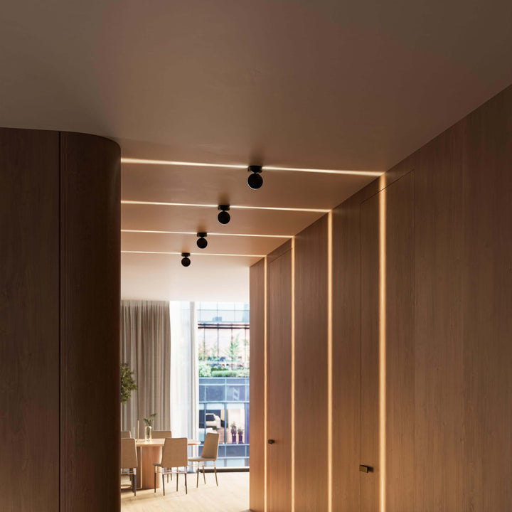 Appliques noires au plafond d'un couloir en bois, lignes de lumière chaude sur les panneaux muraux, vue sur la salle à manger. 15