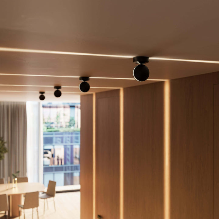 Rangée d'appliques noires au plafond d'un couloir boisé, lignes de lumière chaude sur le plafond et les panneaux muraux. 12