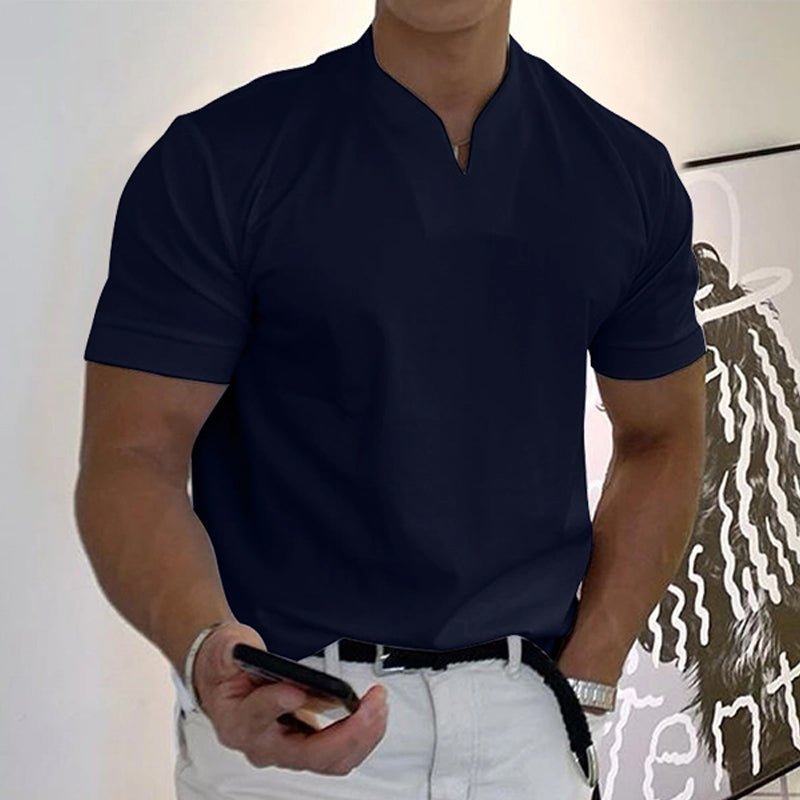 T-shirt bleu marine foncé à col V porté avec un pantalon blanc et une ceinture tressée noire, téléphone en main. 16
