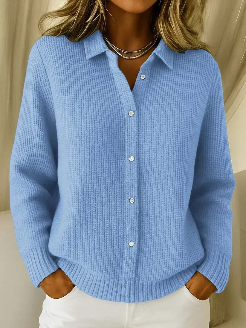 Femme portant le pull en maille texturée bleu ciel, col chemise et boutons blancs, mains dans les poches d'un pantalon blanc. 1
