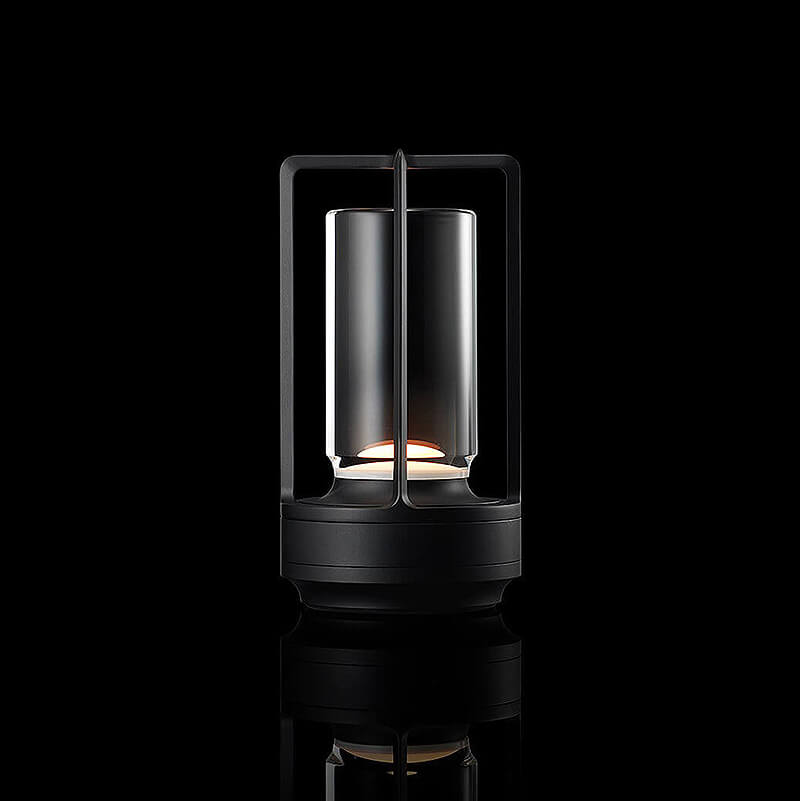 Lampe cylindrique à cadre ouvert et base noirs, allumée sur fond noir avec reflet au sol. 11