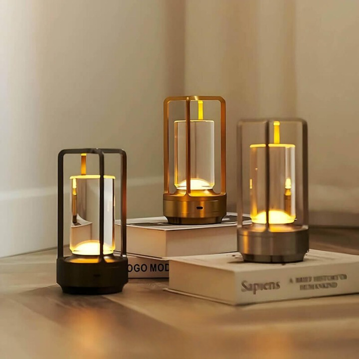 Trois lampes allumées en finitions noire, dorée et argentée, posées sur des livres et un parquet clair. 2