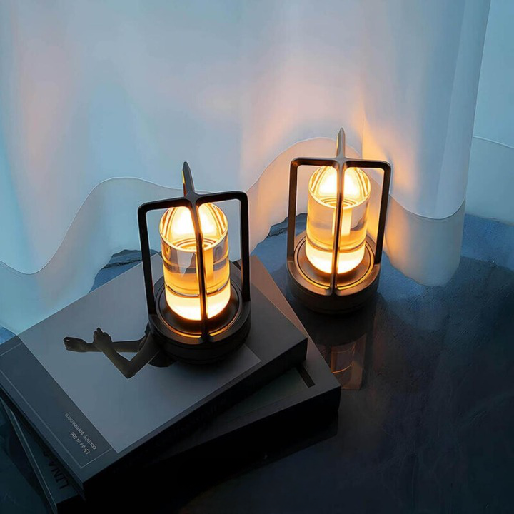Deux lampes à cadre sombre diffusant une lumière chaude, posées sur des livres devant un rideau blanc. 3