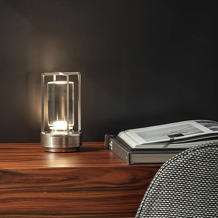 Lampe argentée allumée sur un bureau en bois vernis, à côté de livres d'art, devant un mur sombre. 5