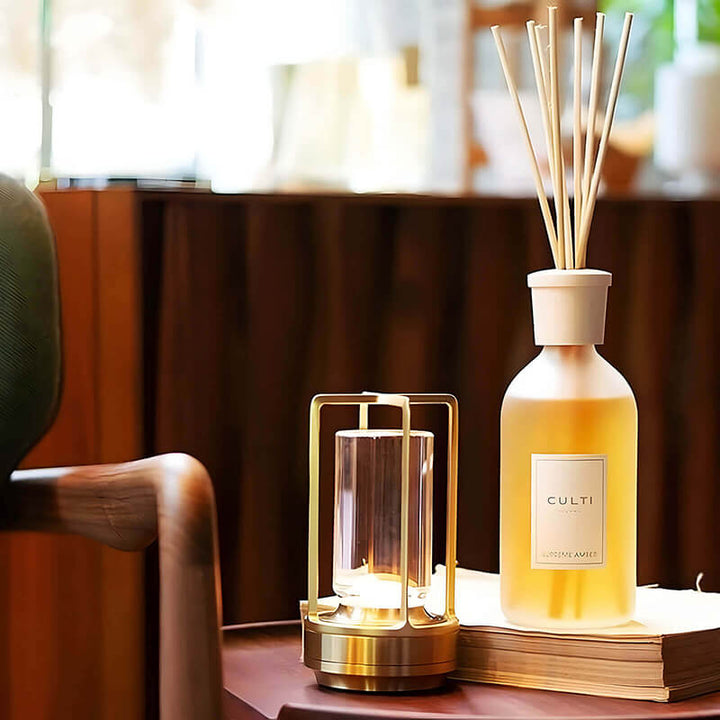 Lampe dorée allumée sur une petite table en bois, à côté d'un diffuseur de parfum à bâtonnets posé sur un livre. 9