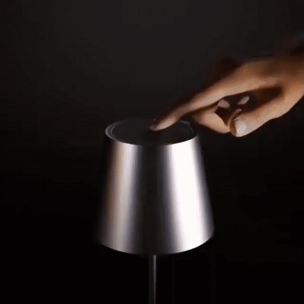 Main qui touche le dessus de l'abat-jour argenté de la lampe pour la commander, sur fond noir. 5