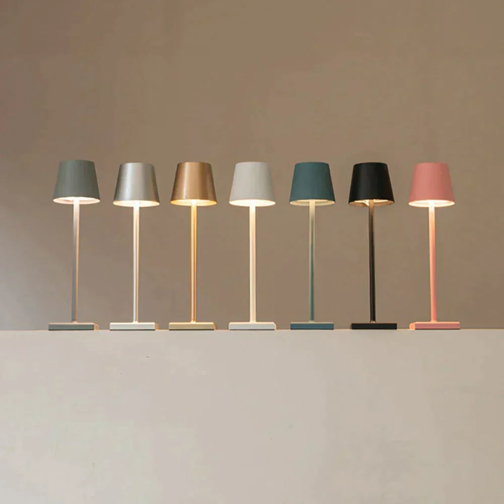 Sept lampes allumées alignées sur un rebord, dans sept coloris : gris, argent, doré, blanc, bleu-vert, noir et rose. 8