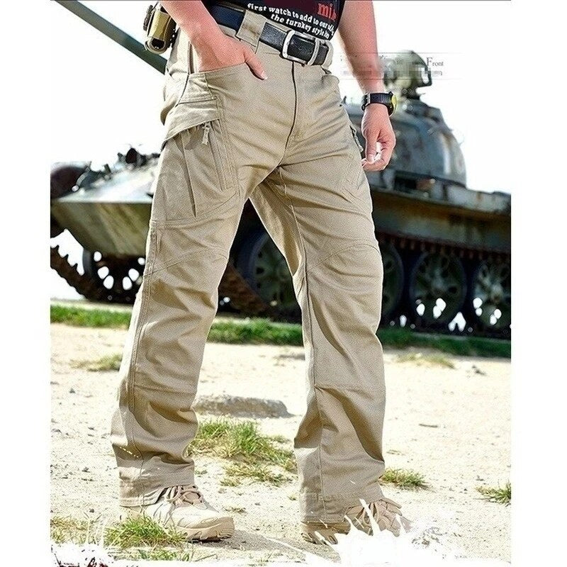 Pantalon cargo beige porté de face, une main dans la poche, en extérieur sur un terrain herbeux devant un char d'assaut. 9