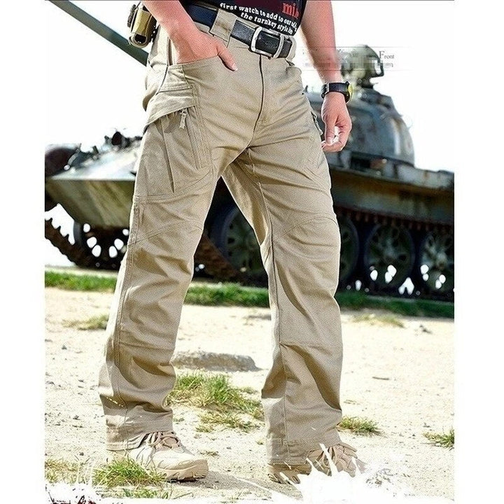 Pantalon cargo beige porté de face, une main dans la poche, en extérieur sur un terrain herbeux devant un char d'assaut. 9