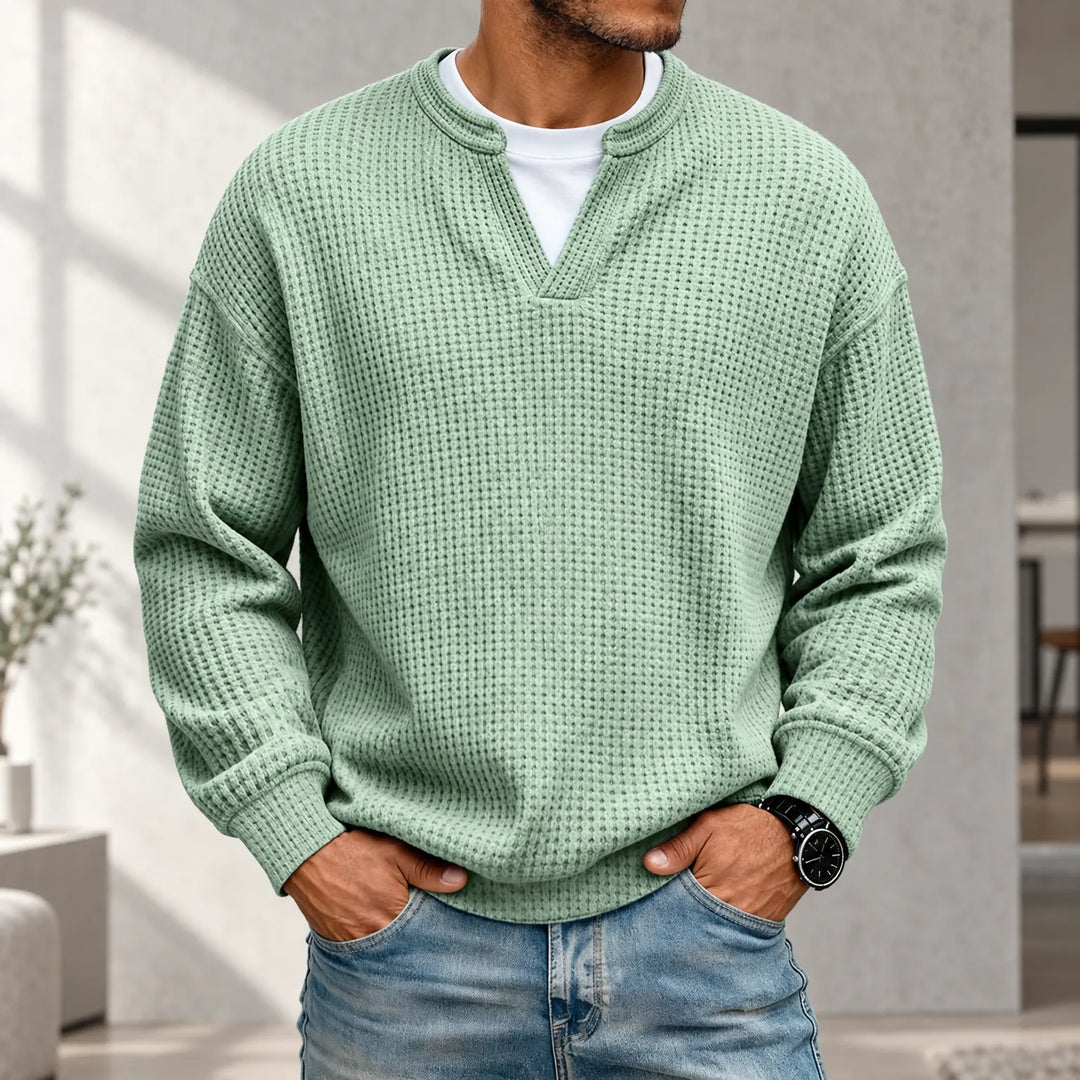 Pull gaufré vert menthe porté par un homme, mains dans les poches, sur t-shirt blanc, devant un décor d'intérieur lumineux. 1