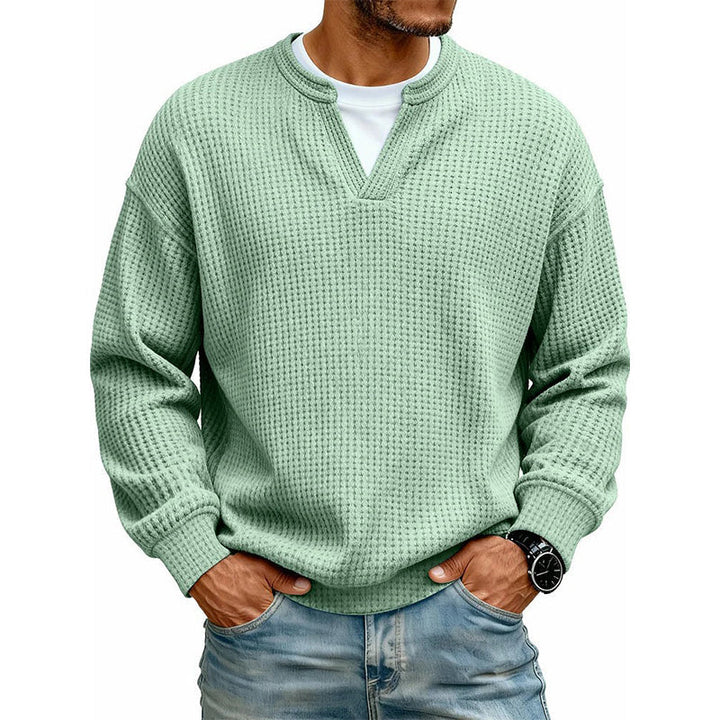 Pull gaufré vert clair porté avec jean et montre noire, mains dans les poches, sur fond blanc. 4