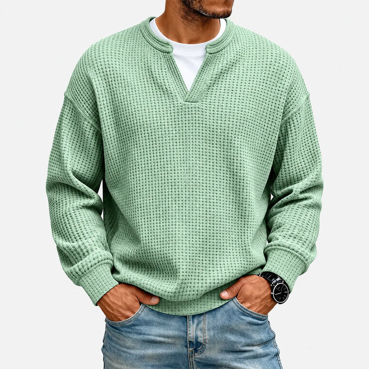 Pull gaufré vert menthe porté par un homme, mains dans les poches de son jean, sur fond blanc uni. 2