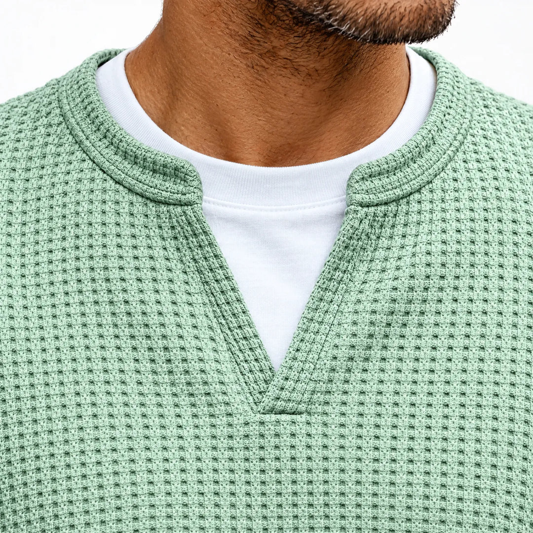 Gros plan sur l'encolure fendue en V du pull gaufré vert, avec un t-shirt blanc en dessous. 3