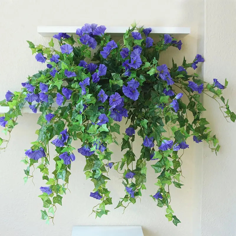 Fleurs artificielles violet-bleu en cascade sur une étagère blanche murale, avec feuilles vertes pendantes le long du mur. 4