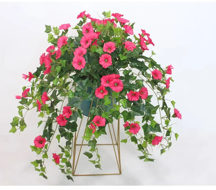 Fleurs artificielles roses et lierre retombant dans un pot posé sur un support doré filaire, sur fond blanc. 3
