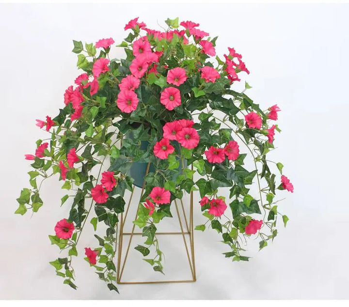 Fleurs artificielles roses et lierre retombant dans un pot posé sur un support doré filaire, sur fond blanc. 3