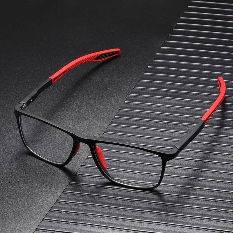 Monture noire aux embouts rouges en silicone, posée en angle sur une surface sombre striée avec un fort contraste. 2