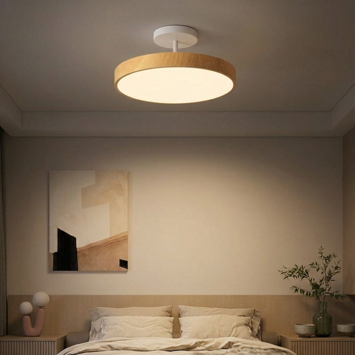Plafonnier à cadre bois clair et platine blanche au-dessus d'un lit, dans une chambre aux tons beiges avec tableau abstrait. 7