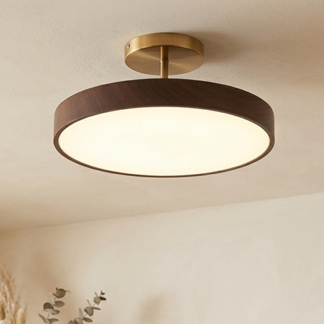 Plafonnier allumé, cadre brun veiné d'aspect noyer et platine dorée, vu en contre-plongée au plafond d'une pièce beige avec feuillage. 1