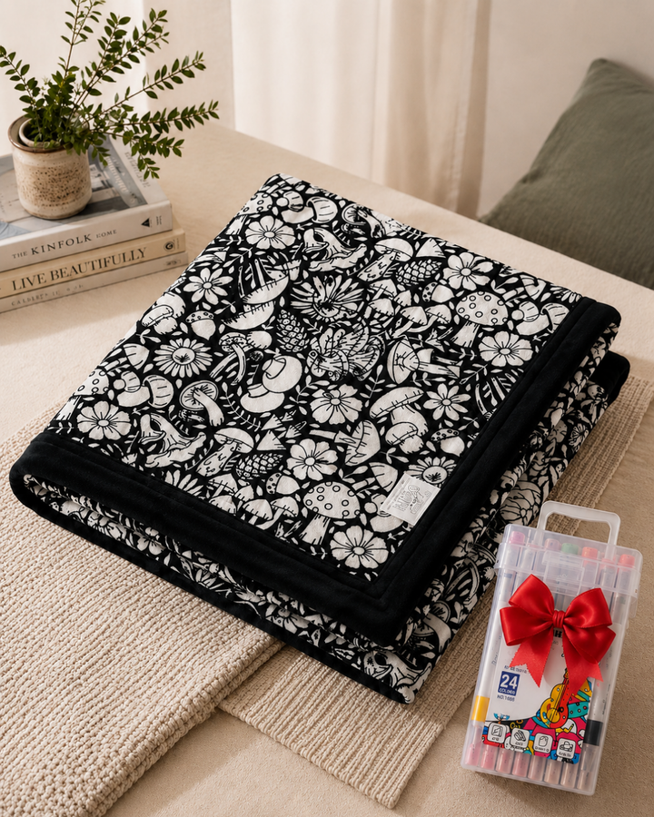 Plaid plié au motif de champignons et de fleurs à colorier, posé à côté d'un coffret de marqueurs 9