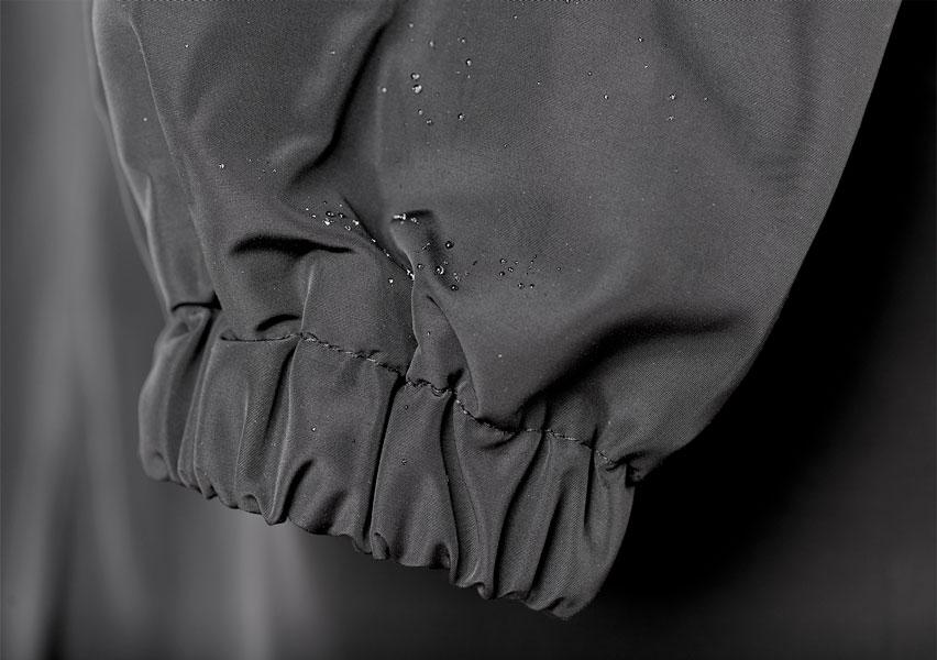 Gros plan sur le poignet élastique froncé d'une manche grise, avec des gouttelettes d'eau qui perlent sur le tissu imperméable. 14
