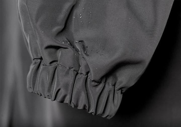 Gros plan sur le poignet élastique froncé d'une manche grise, avec des gouttelettes d'eau qui perlent sur le tissu imperméable. 14