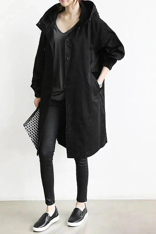 Trench noir à capuche porté de face avec jean noir, baskets noires et une pochette à motif noir et blanc. 5