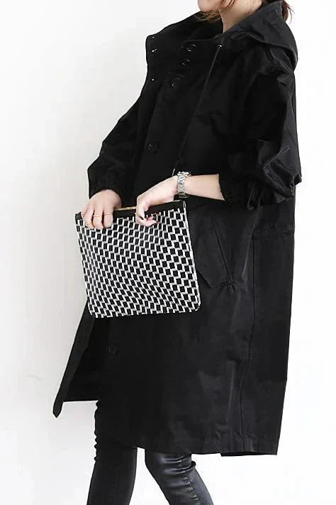 Trench noir vu de profil, porté avec une pochette à motif géométrique noir et blanc tenue devant soi. 6