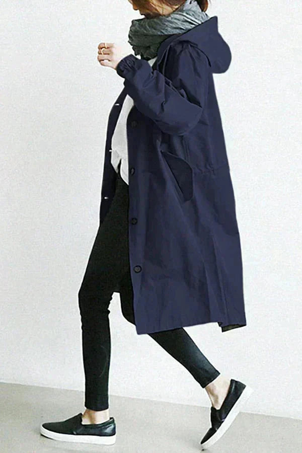 Trench bleu marine à capuche vu de profil, porté en marchant avec écharpe grise, jean noir et baskets. 8