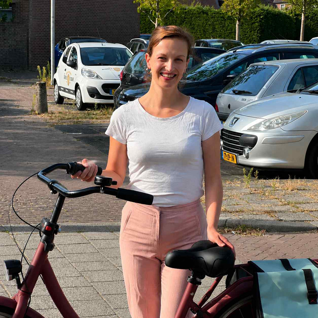 Femme debout près d'un vélo rouge, une main posée sur la selle noire, dans un parking ensoleillé. 7