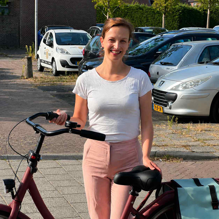 Femme debout près d'un vélo rouge, une main posée sur la selle noire, dans un parking ensoleillé. 7