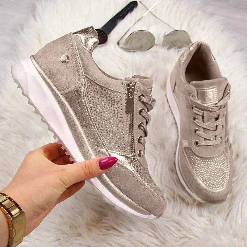 Une main tient une basket beige à zip latéral et semelle blanche crantée, sur un tapis blanc avec lunettes de soleil. 7