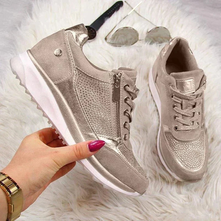 Une main tient une basket beige à zip latéral et semelle blanche crantée, sur un tapis blanc avec lunettes de soleil. 7