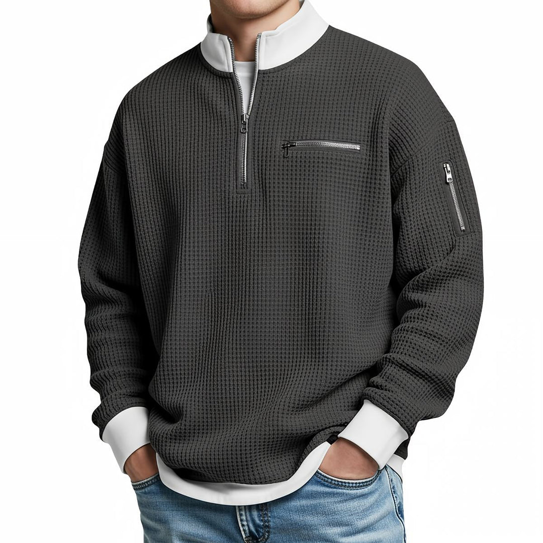 Pull gaufré gris anthracite à col zippé et poche zippée sur la manche, porté de face avec un jean. 9