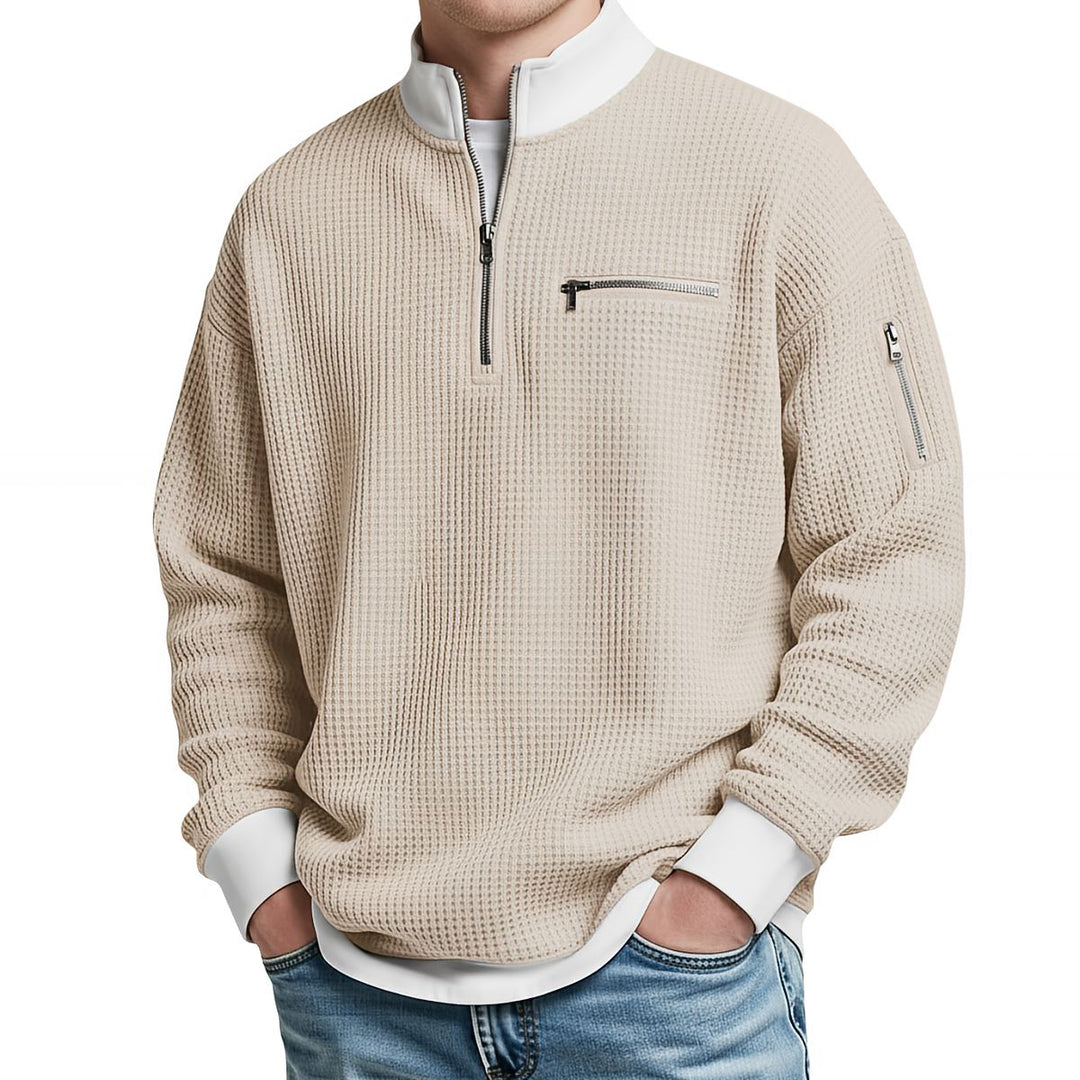 Pull gaufré beige à col zippé, poche zippée sur la poitrine et la manche, porté de face avec un jean. 5