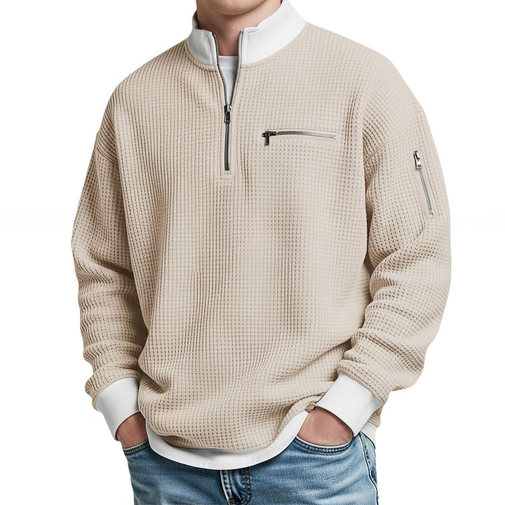 Pull gaufré beige à col zippé, poche zippée sur la poitrine et la manche, porté de face avec un jean. 5