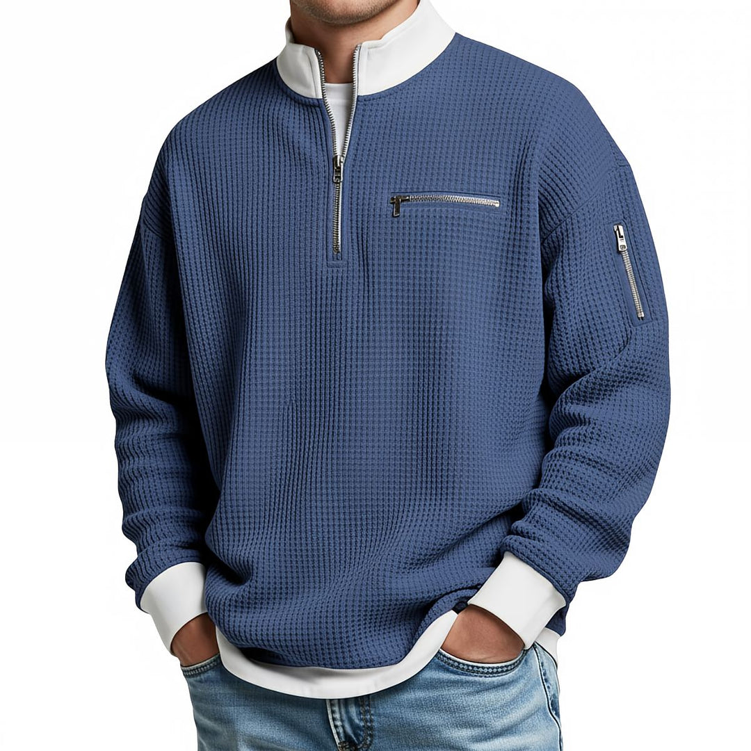 Pull gaufré bleu à col montant zippé, poche poitrine et poche zippée sur la manche, porté avec un jean. 3